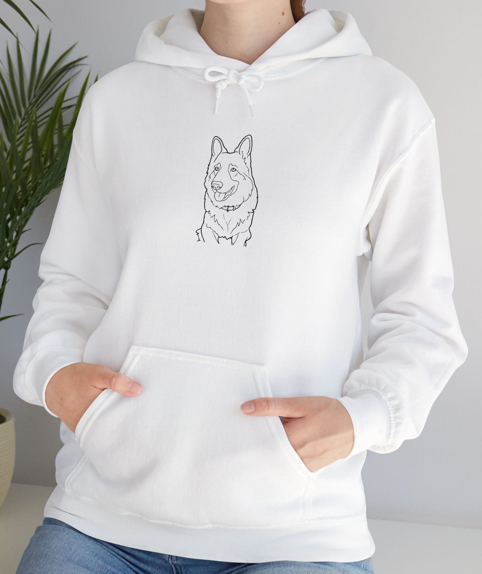 Person wearing a white hoodie with a dog illustration in a room with a plant.