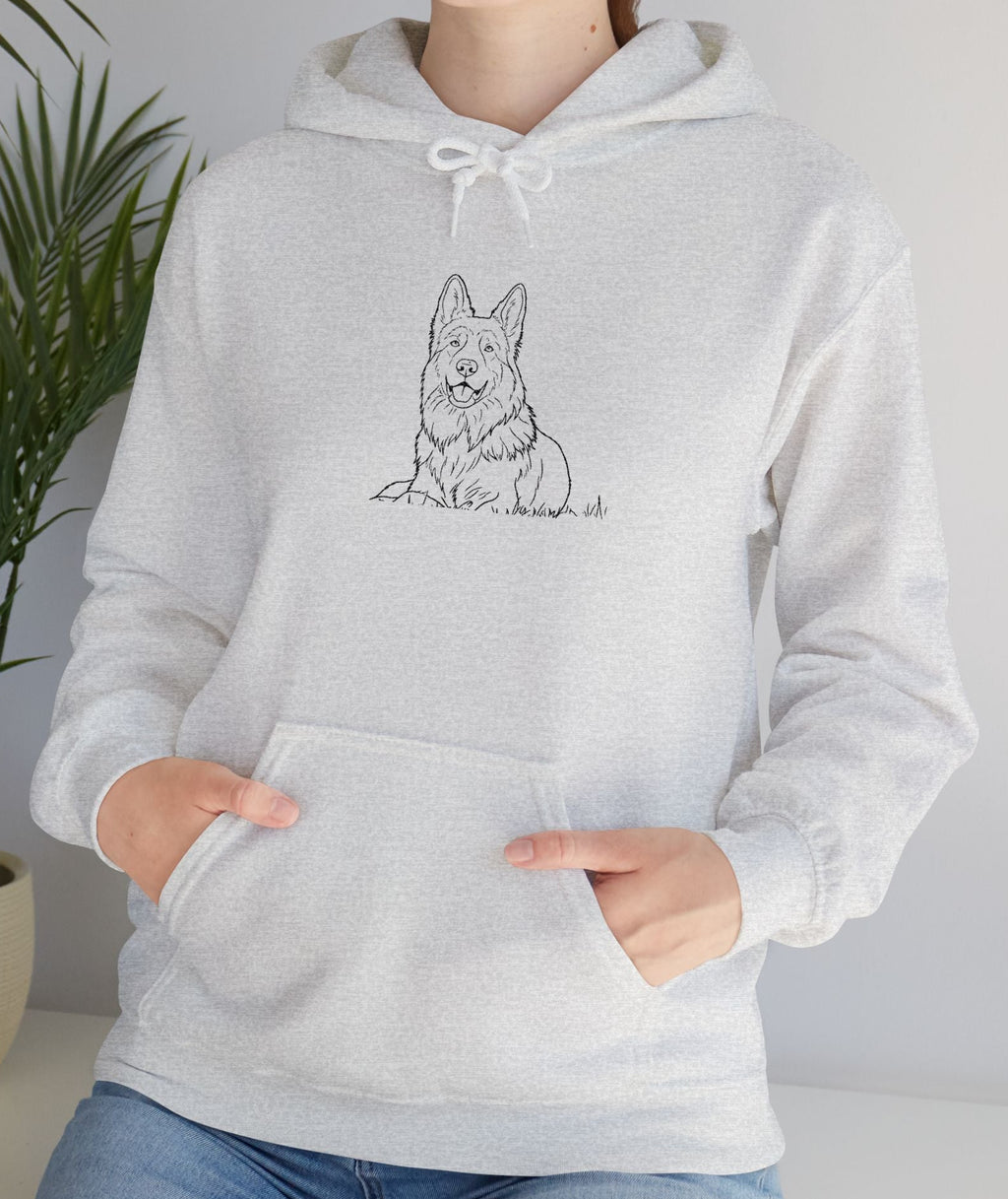 Person wearing a gray hoodie with a dog illustration, standing indoors next to a plant.