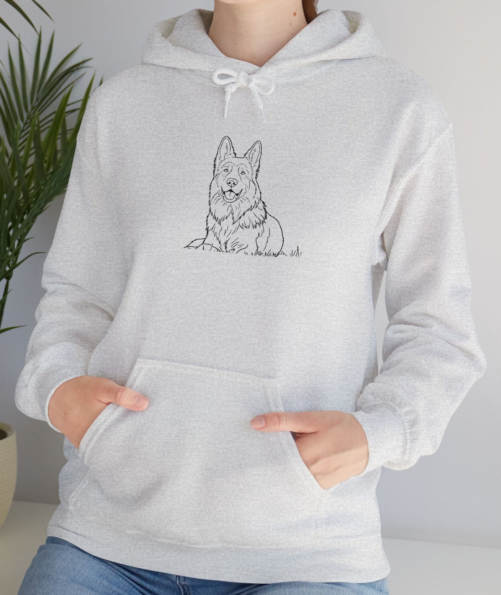 Person wearing a gray hoodie with a dog illustration, standing indoors next to a plant.