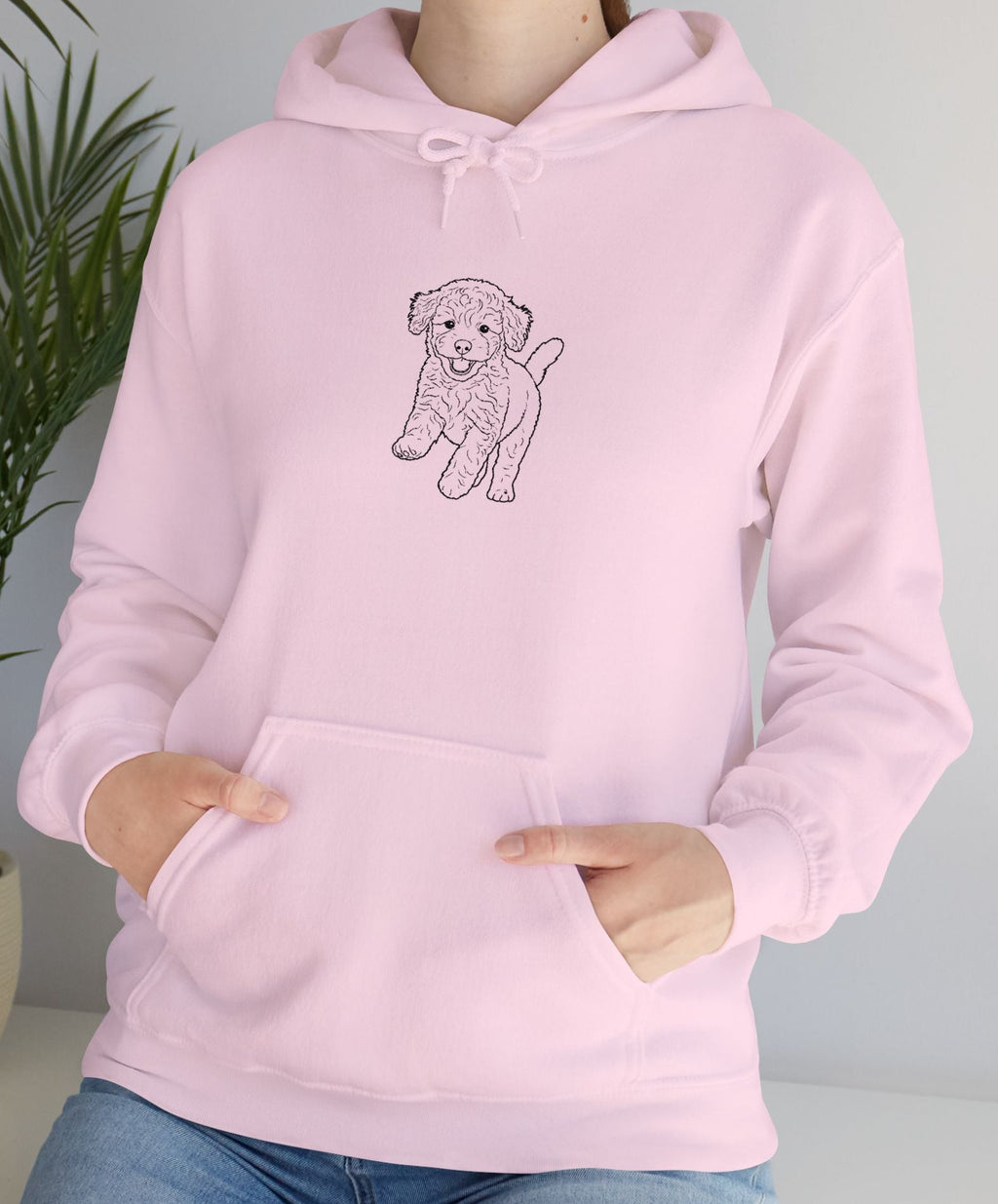 Person wearing a pink hoodie with a dog design, standing indoors next to a plant.