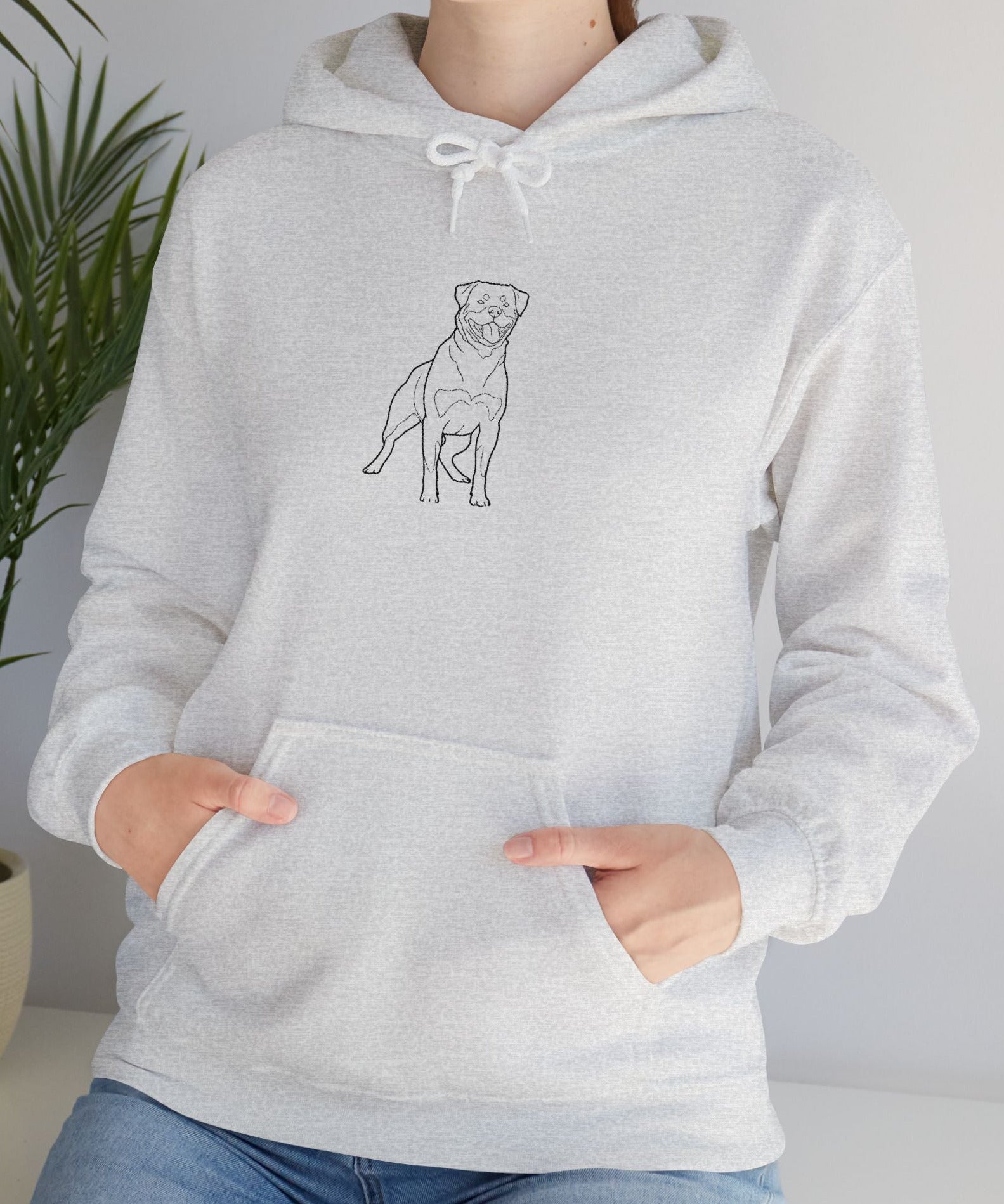 Person wearing a gray hoodie with a dog illustration, standing indoors next to a plant.