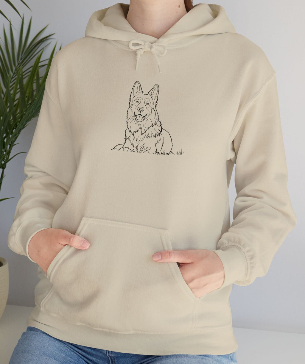 Person wearing a beige hoodie with a dog illustration in front of a plant.