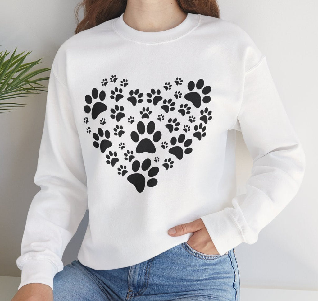 Woman wearing a white sweatshirt with black paw print design, sitting on a white surface with a plant in the background.