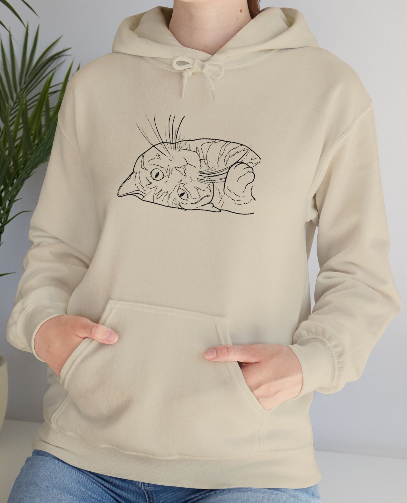 Person wearing a beige hoodie with a graphic design of a cat on a plain background
