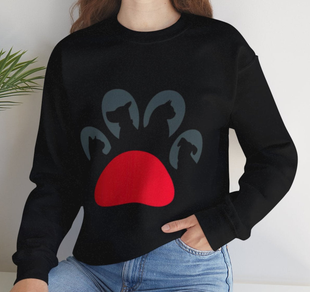 Woman wearing a black sweater with a red and gray paw design, sitting on a white surface with a plant in the background.
