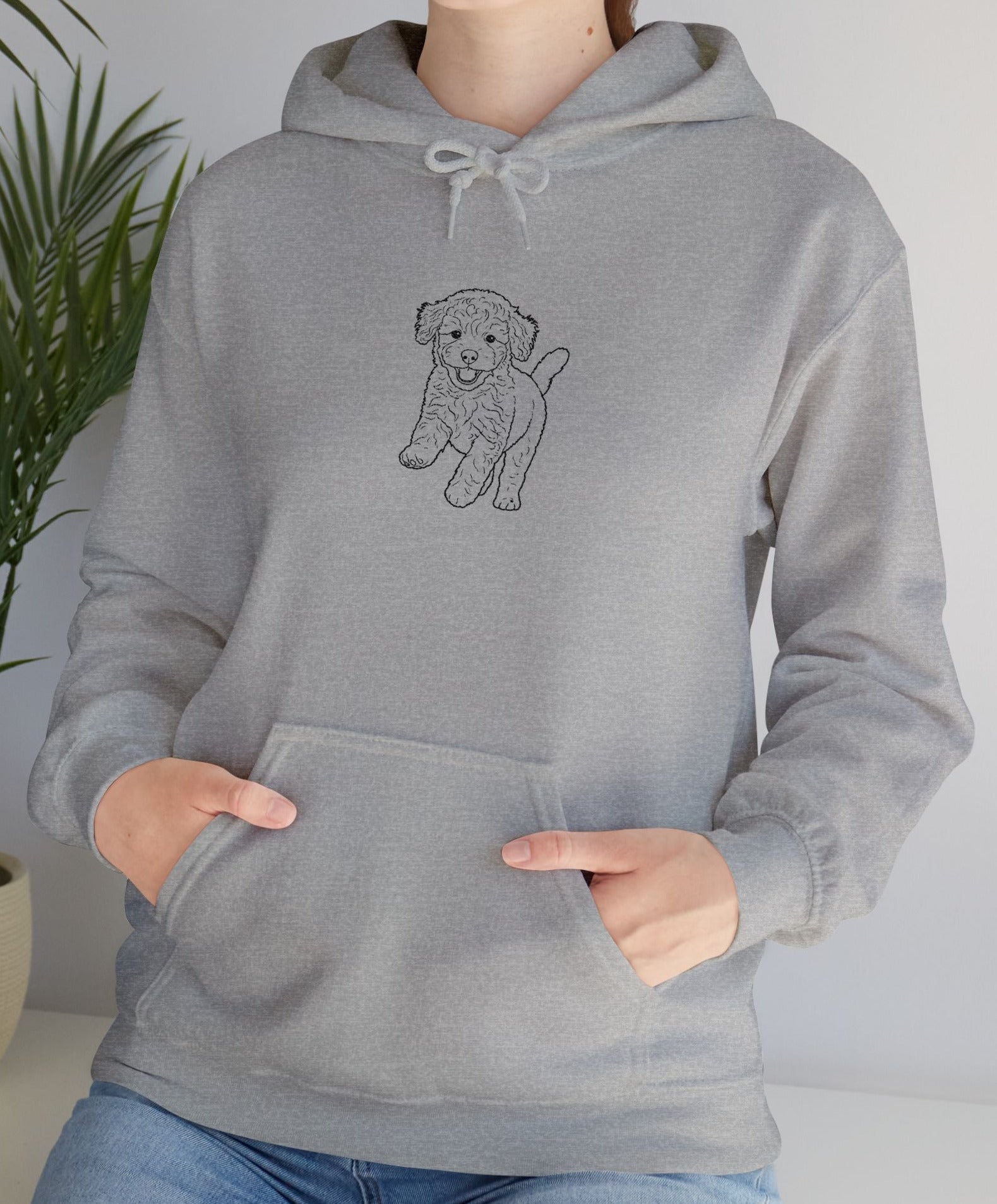 Person wearing a gray hoodie with a dog graphic, standing indoors next to a plant.