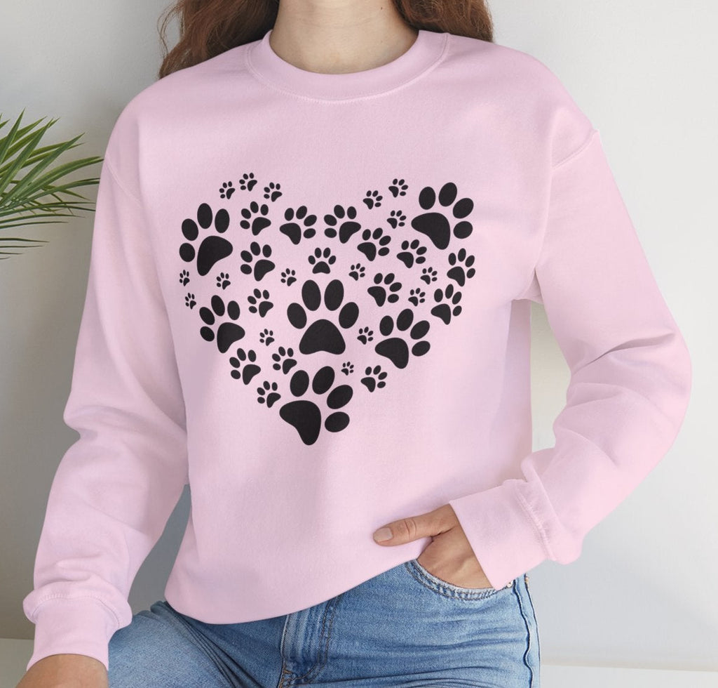 Person wearing a pink sweatshirt with black paw print heart design, sitting on a white surface with a plant in the background.
