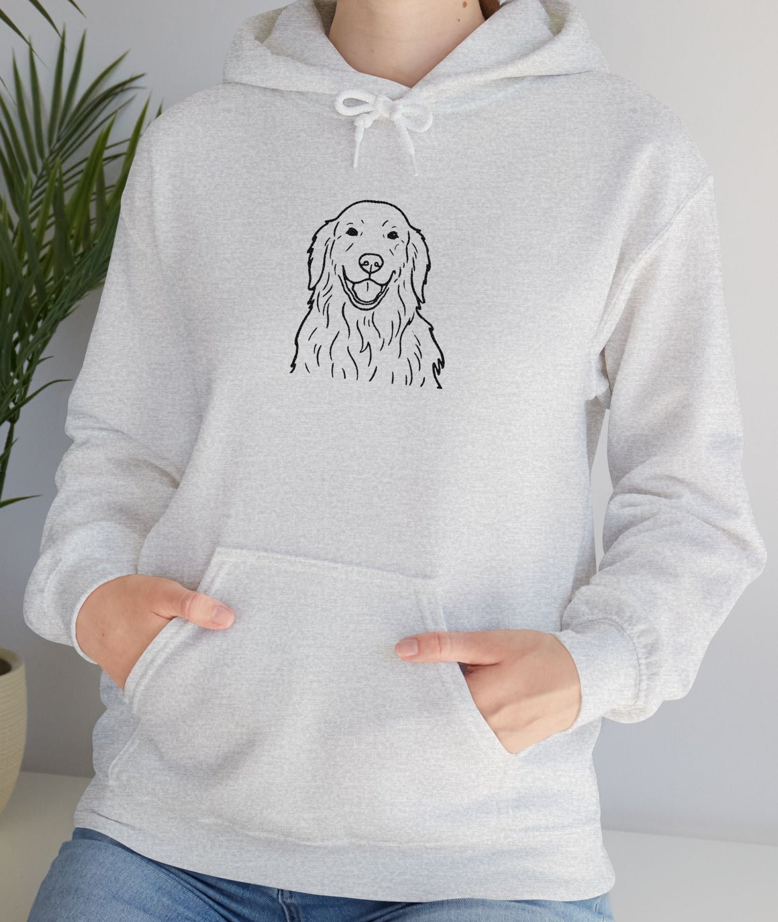 Person wearing a gray hoodie with a dog illustration, standing indoors next to a plant.