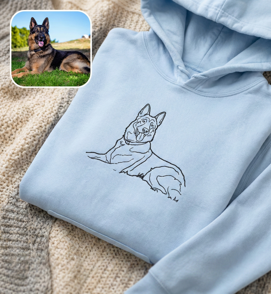 Light blue hoodie with a dog illustration on a textured surface, with a small inset photo of a real German Shepherd.