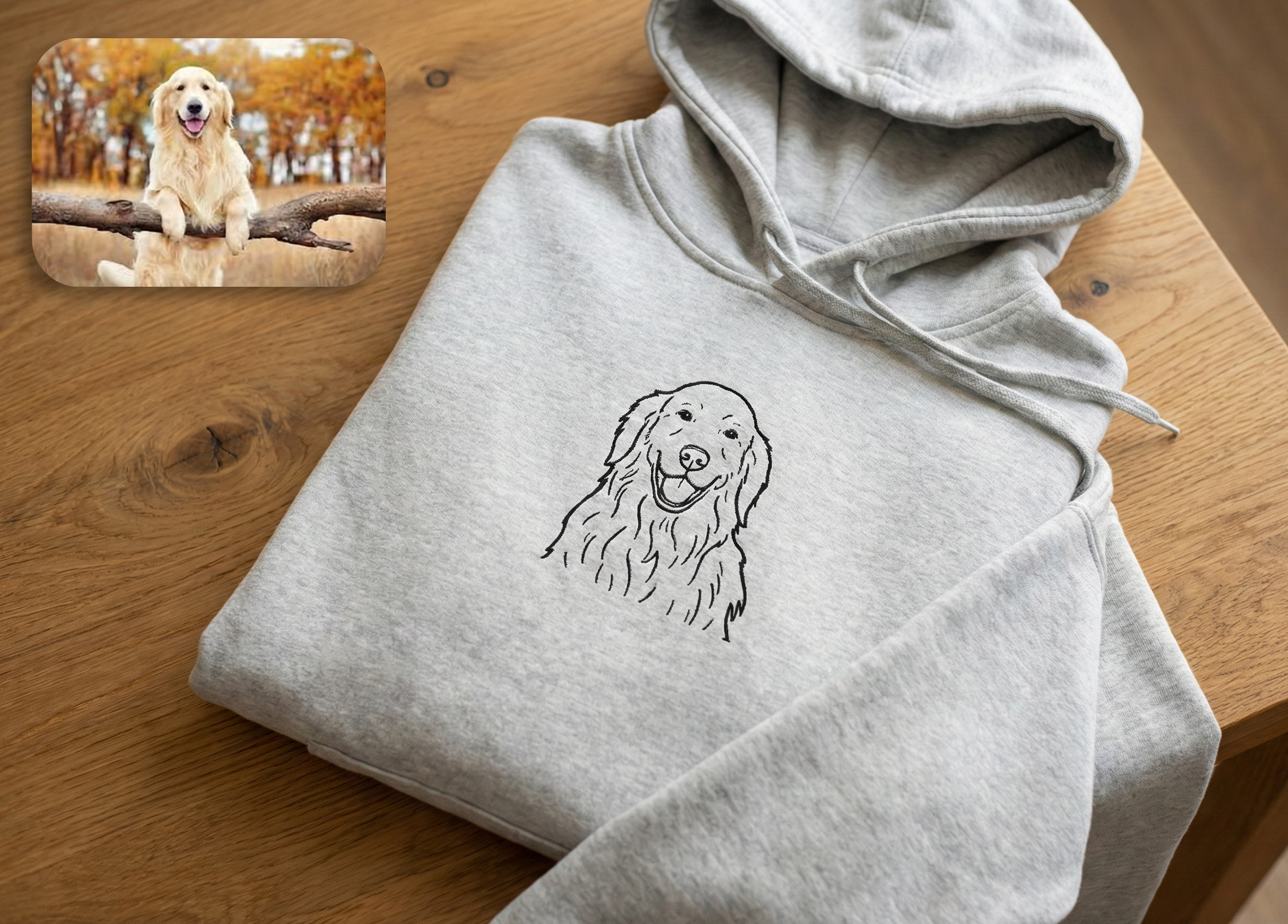 Folded gray hoodie with a dog illustration on a wooden surface, with a smaller inset photo of a dog in nature.