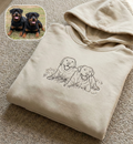 Folded beige hoodie with dog illustration on a carpeted floor, inset showing two Rottweilers.