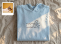 Folded light blue sweatshirt with a cat design on a beige surface