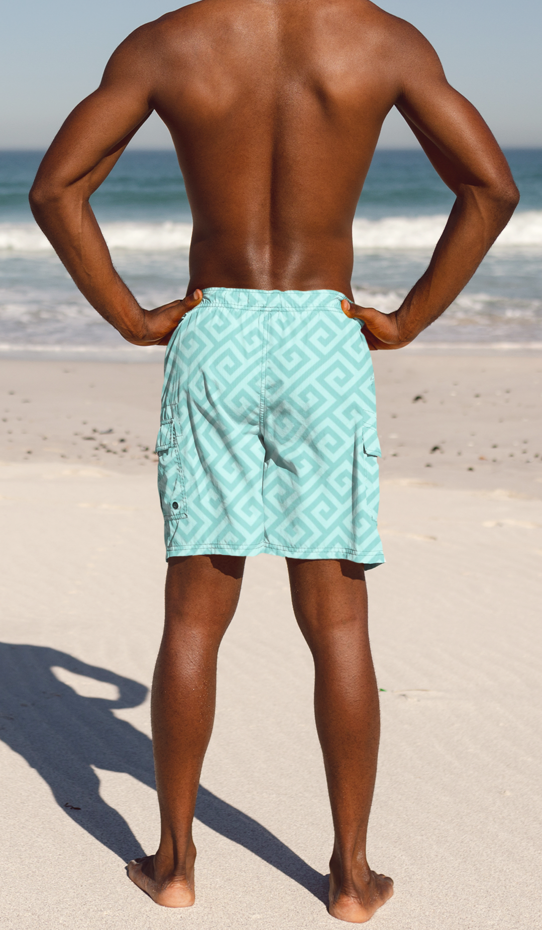Man wearing a teal patterned swim shorts standing on a beach.