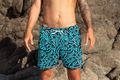 Person wearing blue patterned swim shorts on a rocky beach